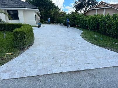 Newly paved driveway with ornamental landscaping and workers showcasing home improvement project.